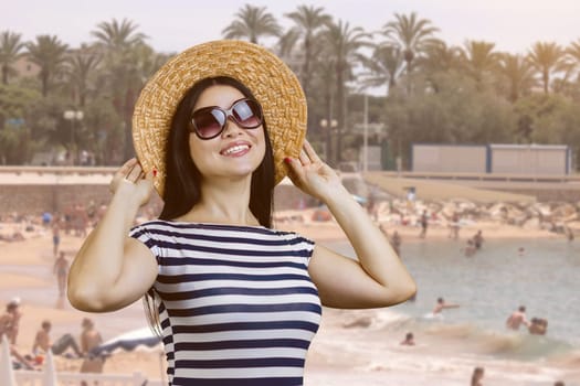 Happy young woman with straw hat standing outdoors. Beach resort background.