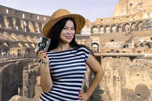 Young asian tourist woman is holding vintage photo camera. Rome Coliseum background.