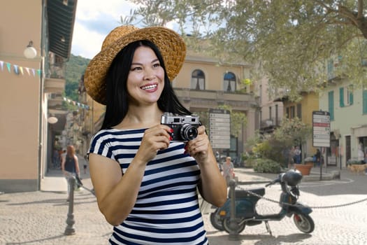 Young cheerful asian womanwith vintage photo camera standing on the street. Female tourist making a photos of sighteeing.