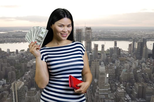 Young asian woman is holding fan of dollars from a red wallet. Urban cityscape background.