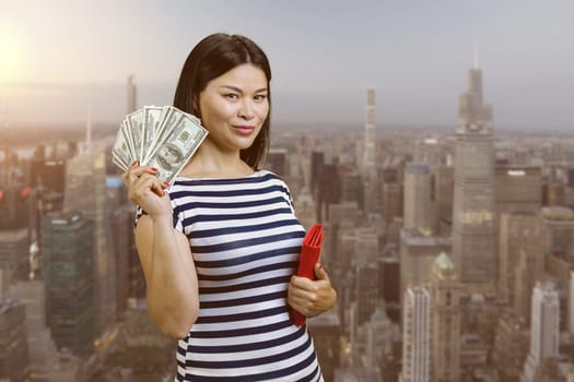 Young korean woman with fan of money from a red wallet. Urban cityscape background.