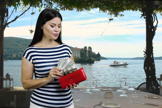 Asian woman is getting dollars from her red wallet on vacation. Summer resort background.