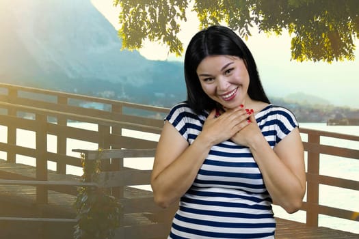 Young asian brunette woman is laughing hard touching her chest with both hands. Summer resort background.