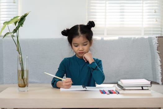Engaged in her studies, a girl thoughtfully writes in her notebook, symbolizing creativity and concentration in her academic endeavors.