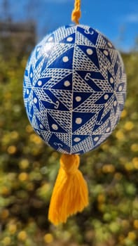 Celebrating traditional Easter, this Ukrainian pysanka features detailed patterns in blue and white. The colorful egg hangs against a backdrop of blooming nature, symbolizing the joy of the season.