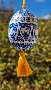 A stunning Ukrainian pysanka decorated with detailed blue patterns and a bright yellow tassel, illustrating traditional Easter celebrations.