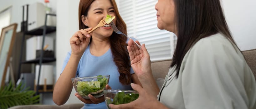 In a cozy living room, the daughter helps her mother with a nutritious salad, illustrating their loving relationship centered around healthy living and wellness.