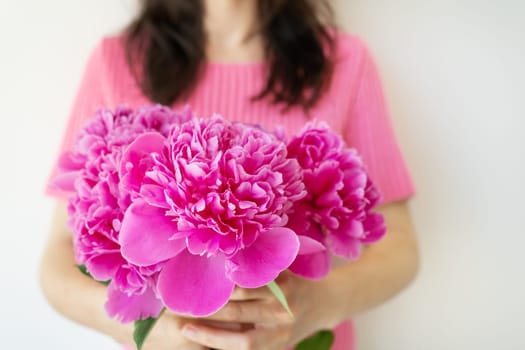 A woman in a pink shirt holds a bouquet of vibrant pink peonies, creating a beautiful and feminine image.