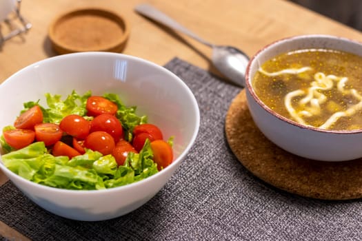 Bawl with cherry tomatoes and lettuce leaves, bawl with soup next to it