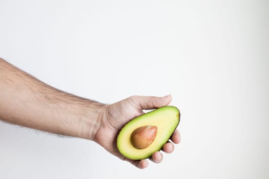 Hand holding half of fresh avocado against white background.