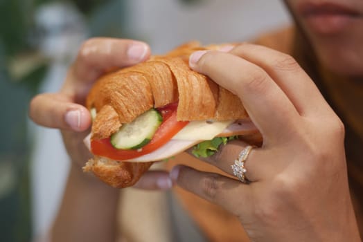 A person holding a croissant sandwich filled with vegetables in a cozy cafe.