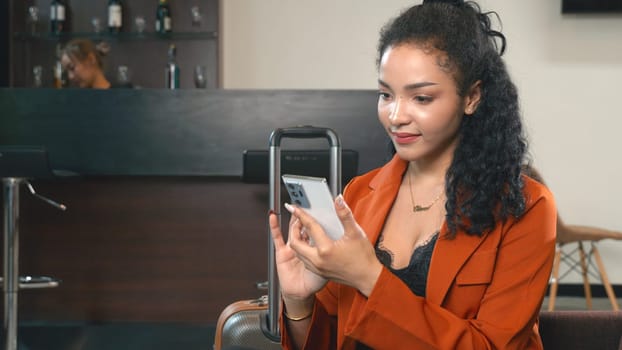 Young beautiful businesswoman with luggage sitting on lounge play smartphone while waiting for boarding of plane in airport, Passenger traveler woman in waiting room check social media on mobile phone