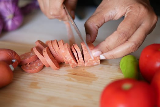 Hands skillfully cut sausage on a wooden board with tomatoes and spices.