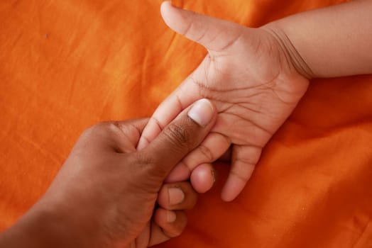 A hand of an adult holds the hand of a child against an orange background.