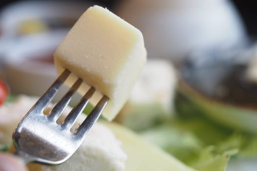 A close-up of a cheese cube balanced on a fork amidst fresh ingredients.