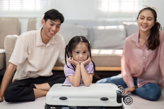 A charming moment unfolds as a girl playfully sits on a suitcase while her parents cheer, illustrating the joy and excitement surrounding their family trip preparations.