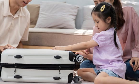 In a cozy living room, a young girl plays with a suitcase, while her parents share joyful moments, emphasizing the importance of family togetherness.