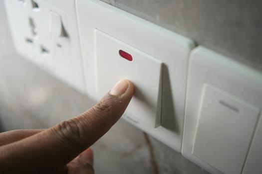A hand presses a modern light switch on a wall, controlling lighting.