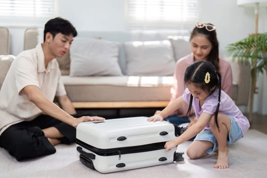 In a cozy living room, a young girl and her parents happily prepare their suitcase for a family vacation, fostering a sense of adventure and connection.