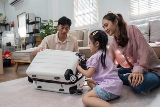 A father and mother enjoy playful interactions with their daughter while she explores a toy suitcase, highlighting the joys of family travel preparations in a cozy home setting.