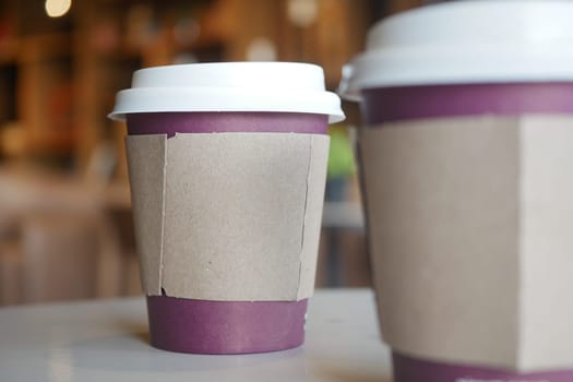 Two paper coffee cups rest on a table in a warm cafe atmosphere.