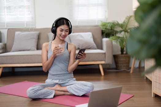 In a serene home environment, the woman practices yoga, connecting with her phone, symbolizing the blend of wellness and technology.