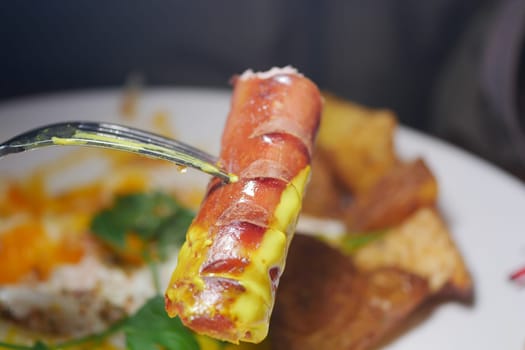 Hot dog with mustard held on fork beside crispy chips and rice.