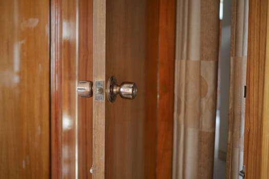 A wooden cabinet door partially open, showing a shiny knob and rich grain.