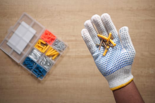 A worker in safety gloves holds screws while a toolbox is visible.