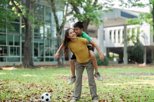 The girl and boy exhibit playful bonding as they enjoy a piggyback ride, a soccer ball rests close by, hinting at their love for outdoor activities.
