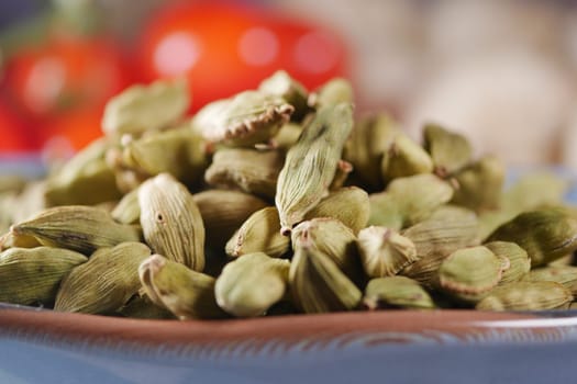 Fresh green cardamom pods are arranged on a plate with tomatoes in background.