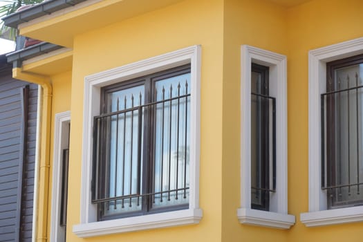 A bright yellow house displays stylish windows with black iron grills.