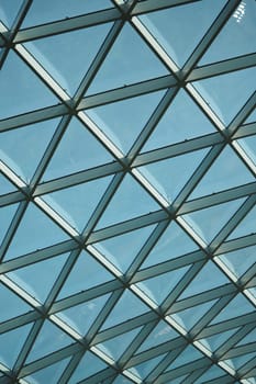 Bright blue sky seen through a geometric glass ceiling during daylight.