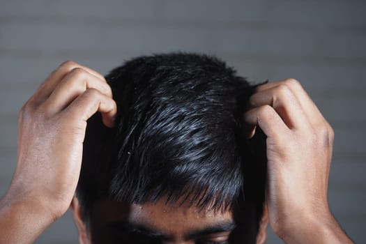 A young man appears stressed, gripping his hair with both hands indoors.
