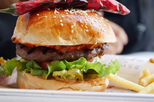 A delicious hamburger with lettuce, tomato, and spicy pepper on top.