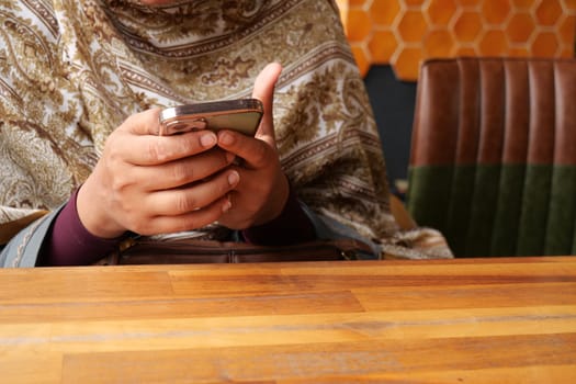Individual is focused on a smartphone at a cafe with wooden decor.