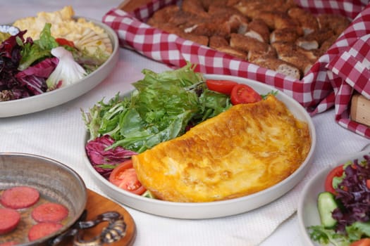 Fresh salad garnished with tomatoes alongside a fluffy omelette and bread.