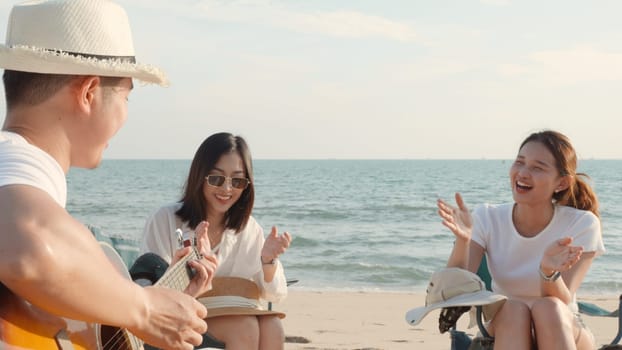 Happy friend have fun playing guitar and clap in camp they smiling together in holiday on sand beach near camping tent vacation time at sunset, Young Asian group woman and man in summer travel outdoor
