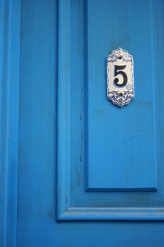 A vibrant blue door features an elegant number five sign.