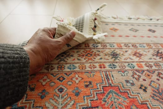 A person smooths a vibrant rug on a polished wooden floor carefully.