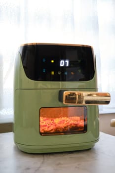 A modern air fryer, designed in a vibrant color, showcases a juicy pork chop cooking to perfection. The digital display shows a timer indicating seven minutes left in the cooking process.