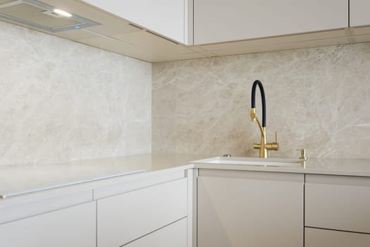 Modern minimalistic kitchen design with light stone surfaces and golden faucet