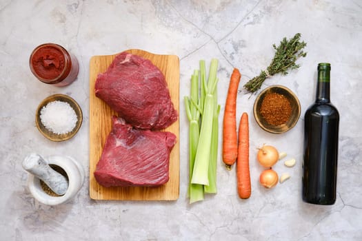 Various fresh ingredients on a kitchen counter, ready for making a beef stew. The setting includes beef meat, vegetables, spices, and a bottle of red wine, inviting culinary creativity.