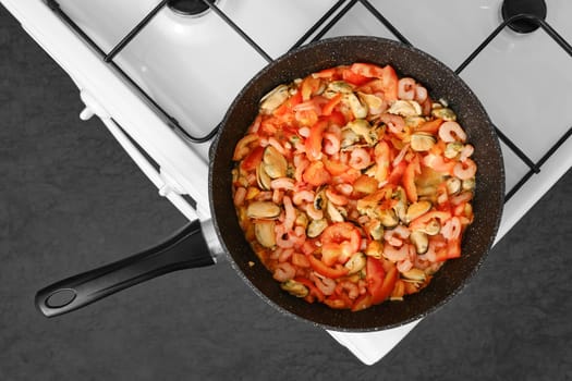 A vibrant stir fry features shrimp, mussels, and sliced tomatoes in a black skillet on a gas stove. The colorful dish captures the essence of cooking seafood, highlighting its freshness and flavor.