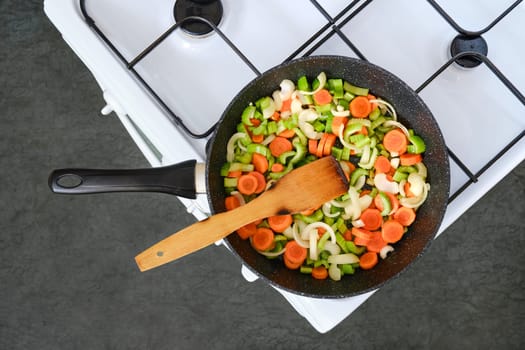 A skillet filled with chopped carrots, celery, and onions on a stovetop. Healthy meal in progress.