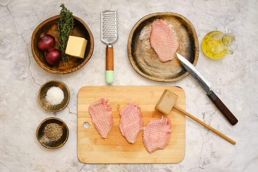 Fresh pork chops are laid out on a wooden cutting board. Surrounding the board are ingredients including onions, butter, herbs, oil, and seasonings, ready for cooking. A knife rests nearby.