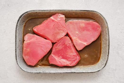 Overhead view of four pieces of raw tuna marinating in soy sauce and lemon juice in a rectangular dish