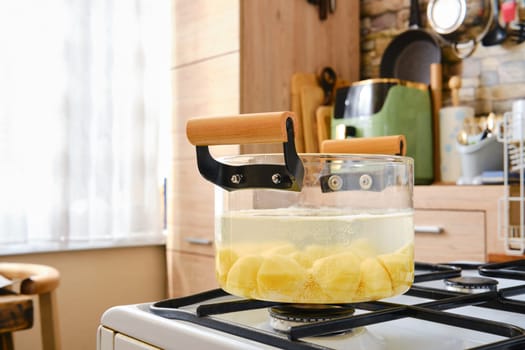 Potatoes cut into pieces simmer gently in a clear pot on a stove.
