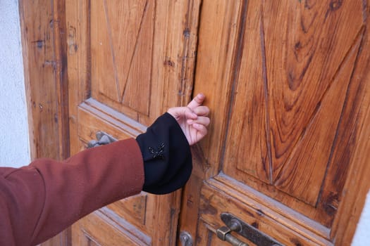A person is poised to knock on a wooden door, showcasing craftsmanship.