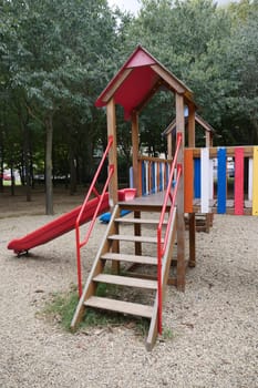 Wooden playground with a slide and vibrant colors surrounded by trees.
